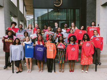 group of graduates holding sweatshirts of their colleges